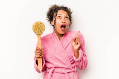 Sırt kaşıyıcı tutan genç İspanyol kadın beyaz arka planda izole edilmiş ve ağzı açık bir şekilde üst tarafı işaret ediyor..