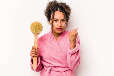 Beyaz arka planda izole edilmiş sırt kaşıyıcı tutan genç İspanyol kadın kameraya yumruk gösteriyor, agresif yüz ifadesi..