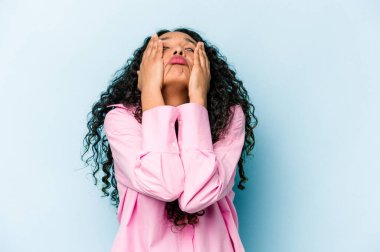 Genç İspanyol kadın mavi arka planda izole edilmiş, ağlıyor, bir şeyden mutsuz, acı ve kafa karışıklığı konsepti..