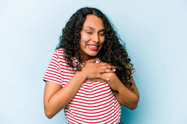 Mavi arka planda izole edilmiş genç İspanyol kadın avuçlarını göğsüne bastıran dostça bir ifadeye sahiptir. Aşk konsepti.