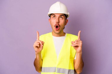 Mor arka planda izole edilmiş genç İspanyol işçi ağzı açık bir şekilde üst tarafı işaret ediyor..