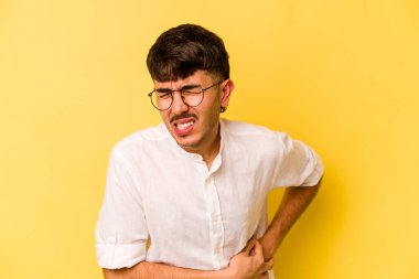 Sarı arka planda karaciğer ağrısı çeken, karnı ağrıyan genç beyaz bir adam..