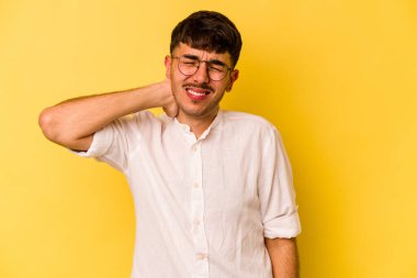 Sarı arka planda izole edilmiş genç beyaz bir adam stresten dolayı boynu ağrıyor, masaj yapıyor ve elle dokunuyor..