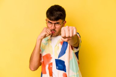 Sarı arka planda izole edilmiş genç beyaz bir adam bir tartışma yüzünden yumruk atıyor, öfkeleniyor, kavga ediyor, boks yapıyor.