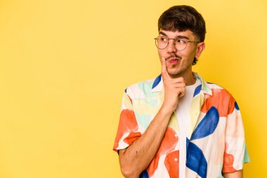 Sarı arka planda izole edilmiş genç beyaz adam şüpheli ve şüpheci bir ifadeyle yana bakıyor..