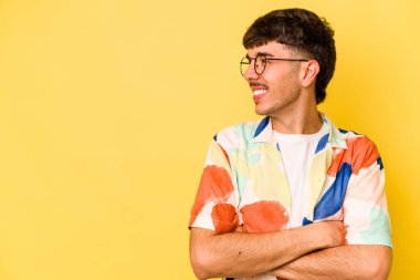 Sarı arka planda izole edilmiş genç beyaz adam kollarını kavuşturarak gülümsüyor..