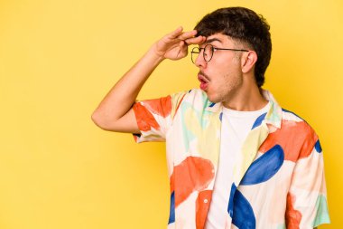 Kafkasyalı genç adam sarı arka planda izole edilmiş, uzaklara bakıyor ve elini alnına koyuyor..