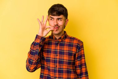 Sarı arka planda izole edilmiş genç beyaz bir adam parmakları dudaklarında bir sır saklıyor..