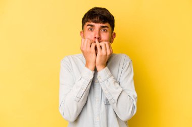 Sarı arka planda izole edilmiş, tırnak yiyen, gergin ve endişeli genç bir beyaz adam..