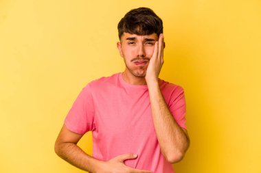 Sarı arka planda izole edilmiş genç beyaz adam yanakları patlatır, yorgun bir ifadeye sahiptir. Yüz ifadesi kavramı.