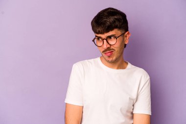 Mor arka planda soyutlanmış, kafası karışmış, şüpheli ve kararsız genç bir beyaz adam..