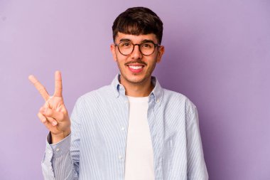 Mor arka planda izole edilmiş genç beyaz adam neşeli ve kaygısız parmakları olan bir barış sembolü gösteriyor..