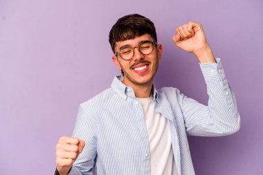 Mor arka planda izole genç beyaz adam özel bir günü kutluyor, atlıyor ve enerjiyle kollarını kaldırıyor..