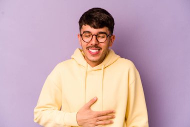 Mor arka planda izole edilmiş genç beyaz adam karnına dokunuyor, nazikçe gülümsüyor, yemek yiyor ve tatmin oluyor..