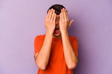 Mor arka planda izole edilmiş genç beyaz adam yüzünün yarısını palmiye ile kaplayarak eğleniyor..