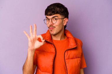 Mor arka planda izole edilmiş genç beyaz bir adam bir göz kırptı ve elleriyle iyi bir jest yaptı..