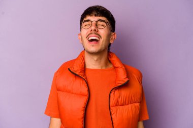 Mor arka planda izole edilmiş genç beyaz adam gevşemiş ve mutlu bir şekilde gülüyor, boynunda dişlerini gösteriyor..