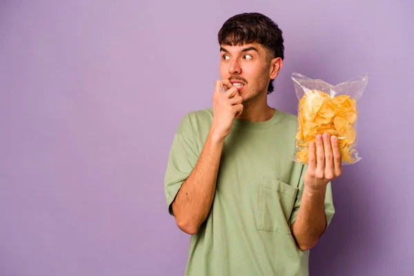 Jonge Spaanse Man Met Chips Geïsoleerd Paarse Achtergrond Ontspannen Denken — Stockfoto