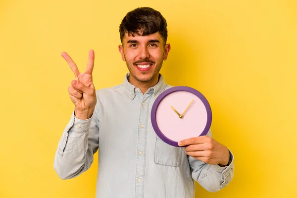 Jovem Hispânico Segurando Relógio Isolado Fundo Amarelo Mostrando Número Dois — Fotografia de Stock