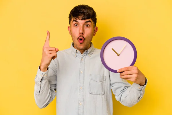 Joven Hispano Sosteniendo Reloj Aislado Sobre Fondo Amarillo Teniendo Alguna — Foto de Stock