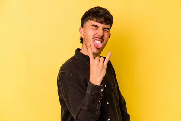Young caucasian man isolated on yellow background showing rock gesture with fingers