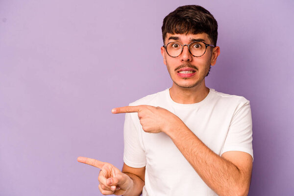 Young caucasian man isolated on purple background shocked pointing with index fingers to a copy space.