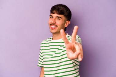 Mor arka planda izole edilmiş genç beyaz adam neşeli ve kaygısız parmakları olan bir barış sembolü gösteriyor..