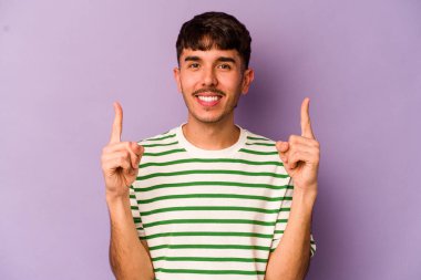 Mor arka planda izole genç beyaz adam iki ön parmağı da boş bir alan gösteriyor..