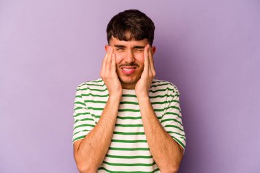 Kafkasyalı genç bir adam mor arka planda izole edilmiş, başı ağrıyor, yüzüne dokunuyor..