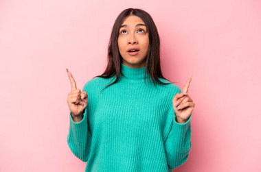 Pembe arka planda izole edilmiş, ağzı açık, üst tarafı işaret eden genç İspanyol kadın..