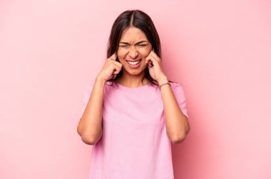 Pembe arka planda izole edilmiş genç İspanyol kadın kulaklarını elleriyle kapatıyor..