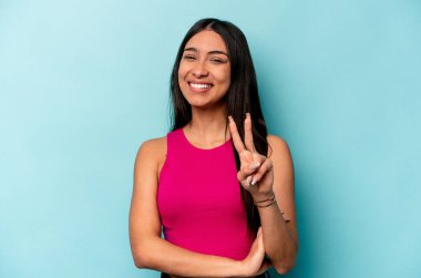 Mavi arka planda izole edilmiş genç İspanyol kadın iki numarayı parmaklarıyla gösteriyor..