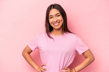 Pembe arka planda izole edilmiş genç İspanyol kadın ellerini kalçasında tutuyor..