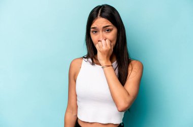 Mavi arka planda izole edilmiş, tırnak yiyen, gergin ve endişeli genç bir kadın..