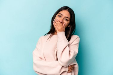 Mavi arka planda izole edilmiş genç İspanyol kadın esniyor. Ağzı eliyle kapatan yorgun bir hareket sergiliyor..