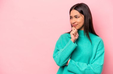 Pembe arka planda izole edilmiş genç İspanyol kadın şüpheli ve şüpheci bir ifadeyle yana bakıyor..