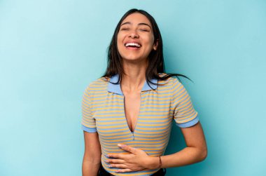 Mavi arka planda izole edilmiş genç İspanyol kadın karnına dokunuyor, nazikçe gülümsüyor, yemek yiyor ve tatmin oluyor..