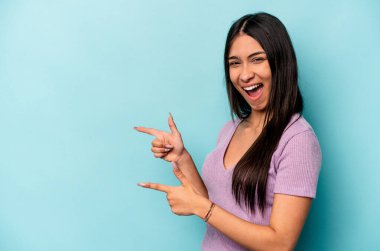 Mavi arka planda izole edilmiş genç İspanyol kadın işaret parmaklarıyla işaret ederek heyecanlanıyor..