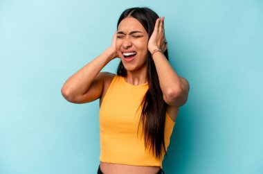 Genç İspanyol kadın mavi arka planda izole edilmiş kulaklarını elleriyle kapatarak yüksek sesle ses duymamaya çalışıyor..