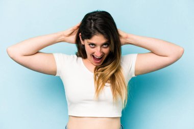 Mavi arka planda izole edilmiş genç beyaz kadın çığlık atıyor, çok heyecanlı, tutkulu, bir şeyden memnun..