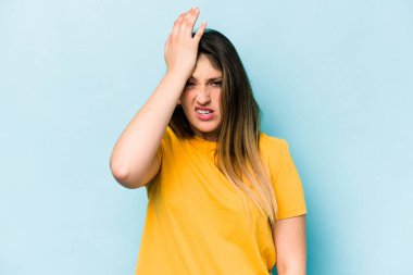 Kafkasyalı genç bir kadın mavi arka planda izole edilmiş bir şekilde bir şeyi unutuyor. Alnına avuç içi ve gözlerini kapayarak vuruyor..