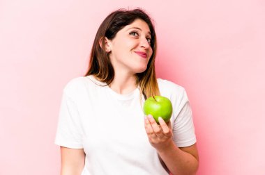 Elma tutan beyaz bir kadın pembe arka planda izole edilmiş hedeflere ve amaçlara ulaşma hayali kuruyor.