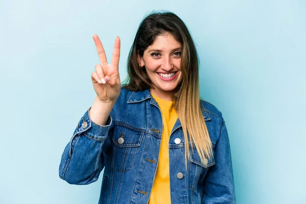 Mavi arka planda izole edilmiş genç beyaz kadın iki numarayı parmaklarıyla gösteriyor..