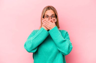 Pembe arka planda izole edilmiş genç, beyaz bir kadın elleri endişeli bir şekilde ağzı örtüyor..