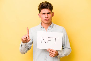 Sarı arka planda NFT levhası tutan beyaz bir adam parmak izi olan bir numarayı gösteriyor..