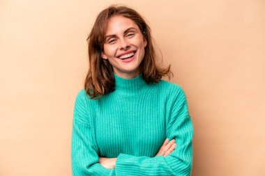 Genç beyaz kadın bej arka planda izole edilmiş gülüyor ve eğleniyor..