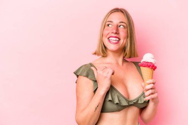 Bikini giyen ve elinde dondurma tutan beyaz bir kadın. Pembe arka planda izole edilmiş, baş parmak uzakta, gülen ve kaygısız..