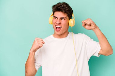 Mavi arka planda izole edilmiş müzik dinleyen beyaz bir adam zaferden sonra yumruğunu kaldırıyor, kazanan konsept..
