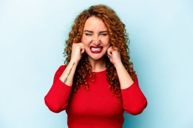 Mavi arka planda izole edilmiş, elleri kulaklarında genç, beyaz bir kadın..