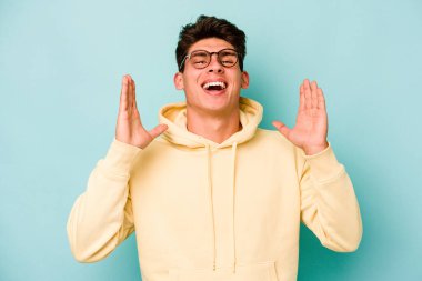 Mavi arka planda izole olmuş genç beyaz adam yüksek sesle gülüyor ve elini göğsüne koyuyor..